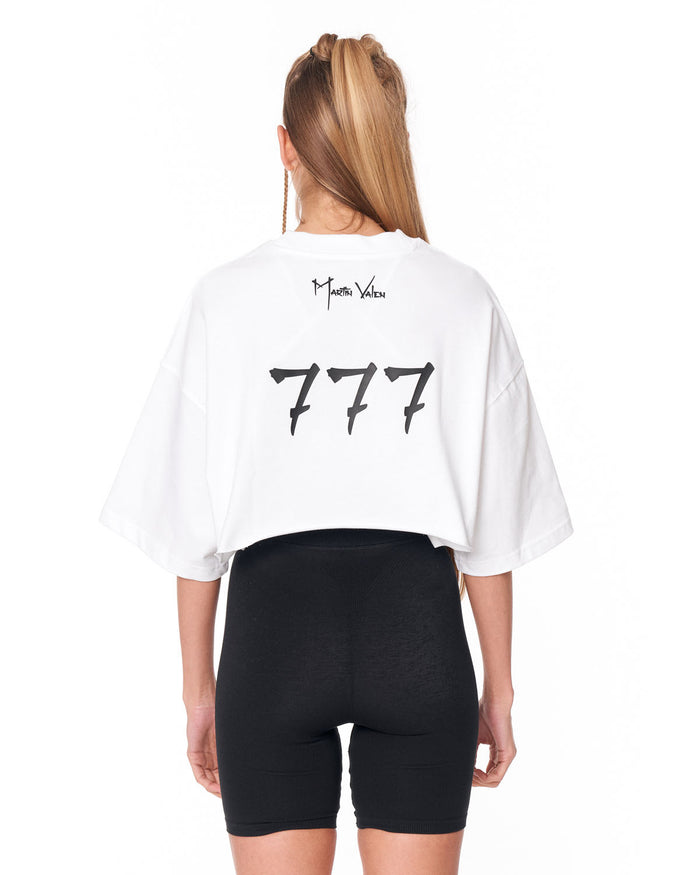 A woman shown from the back wearing a white cropped T-shirt with black '777' graphics and 'Martin Valen' text, paired with black bike shorts, against a plain white background.