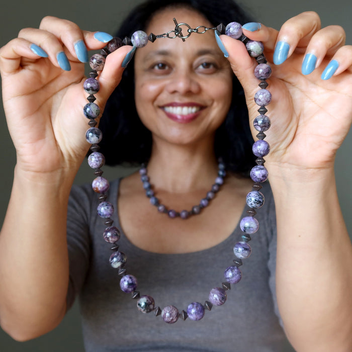 Woman holding a beaded charoite necklace with a gray background