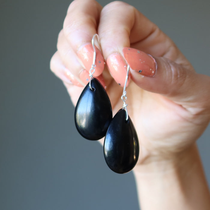 Black teardrop Jet earrings held by a hand against a gray background