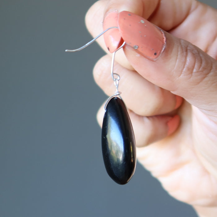Black teardrop Jet earrings held by a hand with pink nail polish against a gray background