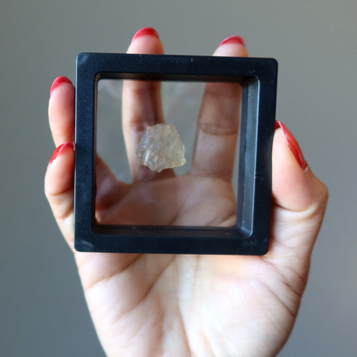 hand holding yellow libyan desert glass tektite in display case