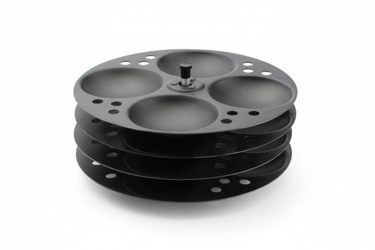 A black non-stick idli stand with four racks, made of stainless steel, designed for making idlis.